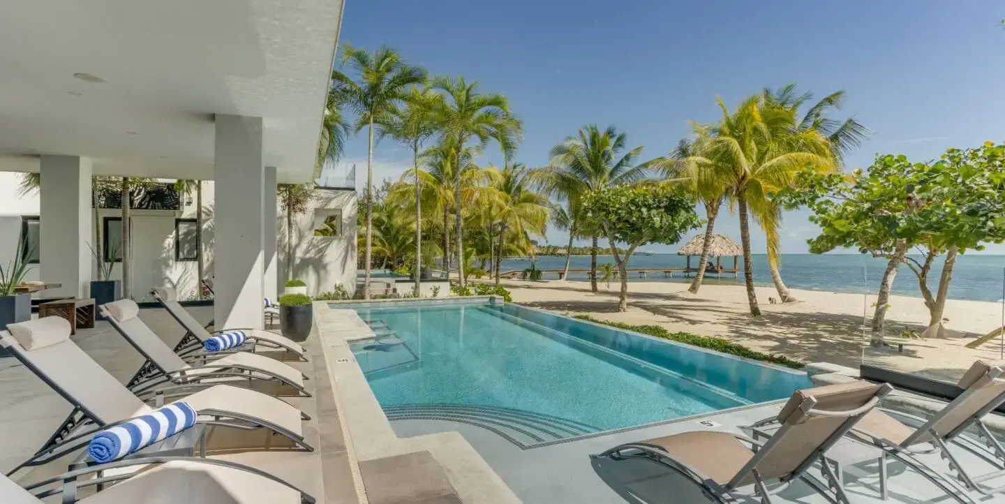 High-angle view of the luxury swimming pool surrounded by tropical palm trees and modern vacation villas at The Villas at Playa de Coco in Belize.